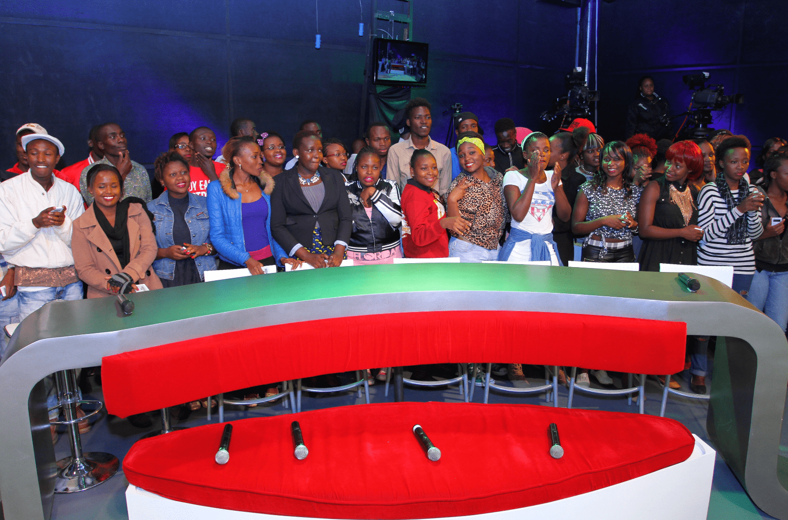 Studio audience standing behind a modern red and silver desk